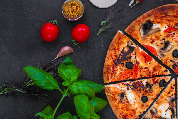 pizza con pepperoni, tomates, queso y albahaca sobre un fondo negro. vista superior.  - Foto, imagen