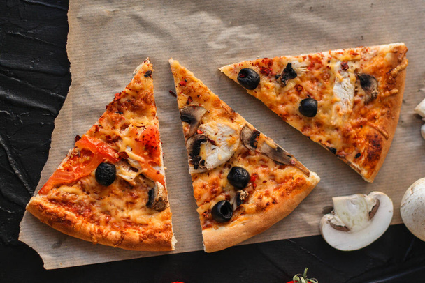 Pizza mit Paprika, Tomaten, Käse, Pilzen und Oliven auf schwarzem Hintergrund. Ansicht von oben. - Foto, Bild