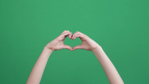 Detailní záběr dětských rukou, které dělají gesto tvaru srdce na zeleném pozadí obrazovky chromakey. Osoba vytváří tvar srdce pomocí prstů - Záběry, video