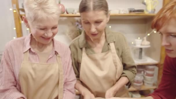 手作りの陶器の器をチェックする若い女性の工芸教師の中撮影と彼女の創造的なワークショップで陶器のレッスン中に2人の高齢者の白人女性に助言を与える - 映像、動画
