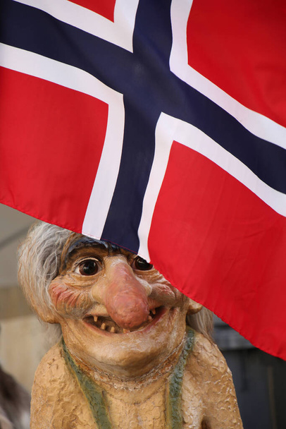 Posąg trolla, który jest tradycyjnym norweskim folklorem stojącym pod czerwoną, białą i niebieską flagą Norwegii.  - Zdjęcie, obraz