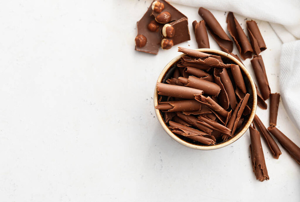 Kıvrımlı kase ve açık arkaplanda çikolata parçaları - Fotoğraf, Görsel