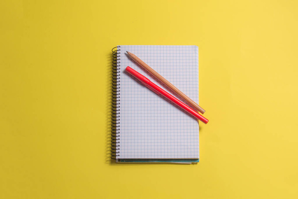 блокнот з олівцем і ручкою, ізольований на жовтому фоні
 - Фото, зображення