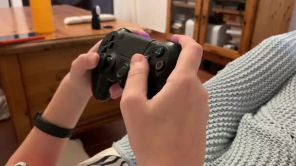 Een tiener speelt een spelcomputer met een joystick terwijl hij thuis op de bank zit. Achteraanzicht van het kind liggend op de bank tijdens quarantaine heeft plezier met het spelen van moderne games op een console. - Video