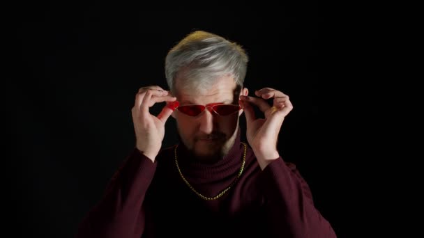 Портрет соблазнительного молодого человека в модной стильной одежде в красных солнечных очках на черном фоне - Кадры, видео