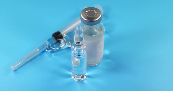 Skleněná injekční lahvička naplněná modrou tekutou vakcínou a injekční stříkačkou se otáčí na velmi modrém pozadí. Farmaceutický průmysl. Léčba virové infekce. Zpomalený pohyb. - Záběry, video