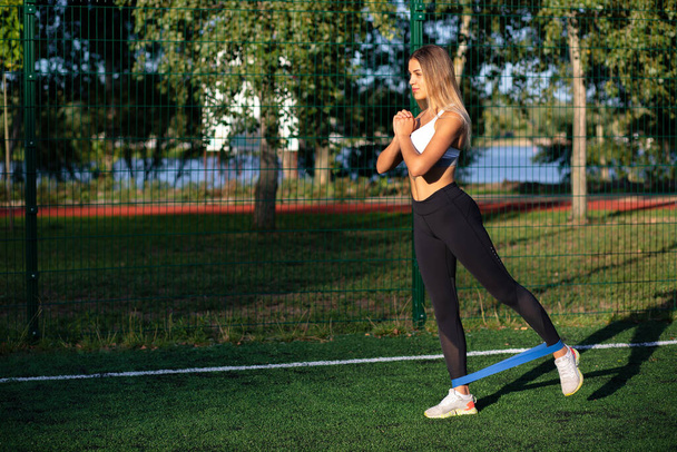 Zmotywowana sportowa kobieta ćwicząca z gumą do ćwiczeń na boisku. Miejsce na tekst - Zdjęcie, obraz