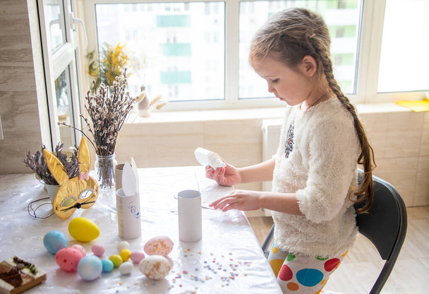 La chica pega las orejas del conejo de Pascua, la preparación para la Feliz Pascua, la creatividad de los niños, coloridos huevos pintados brillantes en la mesa. - Foto, imagen