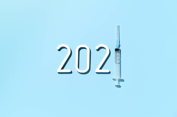 Das Jahr 2021 - das Jahr der Massenimpfung gegen COVID-19 der Weltbevölkerung, das Konzept des Sieges über das Coronavirus. Draufsicht auf Datum 2021, Spritze auf pastellblauem Hintergrund - Foto, Bild