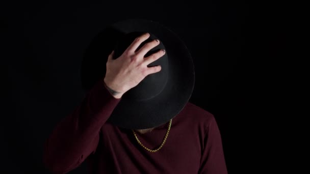 Портрет соблазнительного улыбающегося молодого человека в модной стильной одежде в шляпе на черном фоне - Кадры, видео