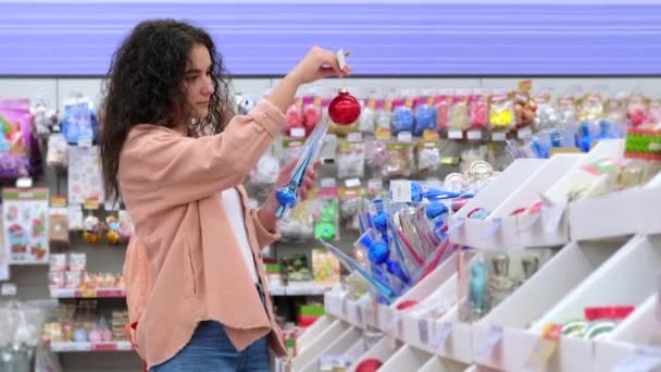 naispuolinen asiakas valitsee kiiltävä joulukoriste puu ja sisätilojen huoneisto supermarketissa - Materiaali, video