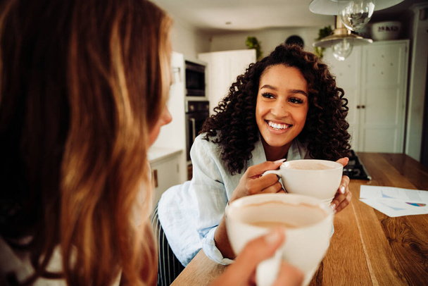 Mixed race friends laughing together in kitchen drinking hot coffee  - Fotoğraf, Görsel