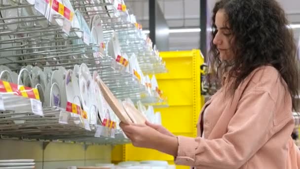 morena mujer está eligiendo placas de cerámica en el supermercado - Metraje, vídeo