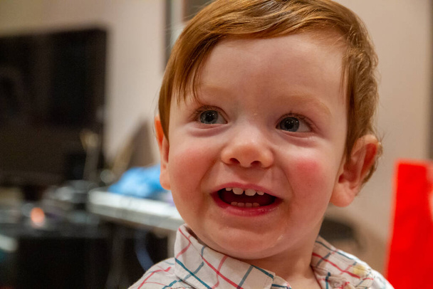 Egy cuki, vörös hajú, kék szemű kisfiú portréja, aki mosolyog és a kamerába néz - Fotó, kép