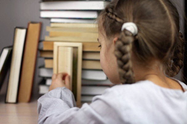 Έξυπνο χαριτωμένο κορίτσι που ανοίγει μια μικρή πόρτα στο σπίτι των βιβλίων, δέσμη των φώτων μέσα από την πόρτα - Φωτογραφία, εικόνα