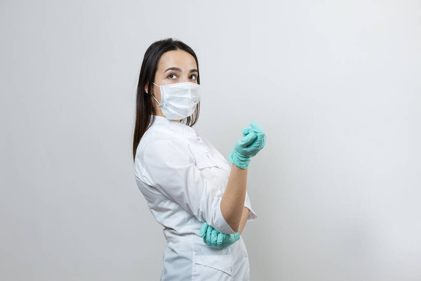 Ένα κορίτσι γιατρός σε γάντια λάτεξ και ένα λευκό παλτό ετοιμάζεται για τις διαδικασίες. - Φωτογραφία, εικόνα