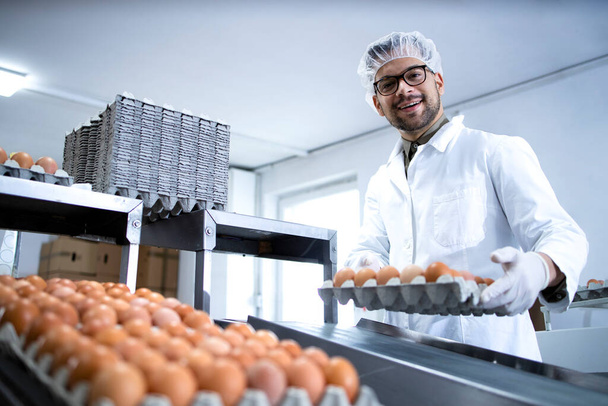 Trabajador de la fábrica que trabaja en la línea de producción de alimentos con cajas llenas de huevos frescos preparándolos para la venta. Planta de procesamiento de alimentos ecológicos. - Foto, Imagen