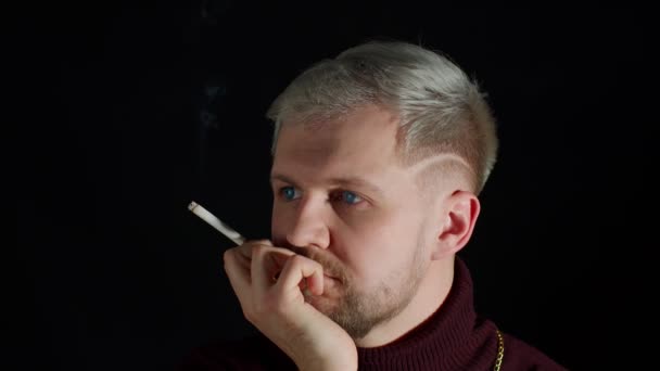 Elegante joven adicto con ojos azules en la ropa de moda mirando a la cámara, fumar cigarrillo - Metraje, vídeo