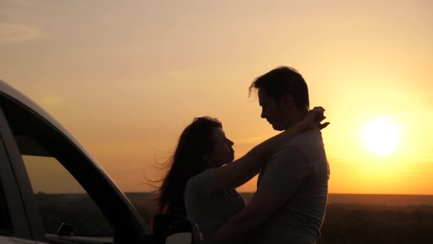 Happy enamored travelers man and woman stand next to car and admire beautiful sunset at campsite. Tourists travel by car, hug, admire sunrise, nature. Free travelers, tourists. Family travel by car. - Footage, Video