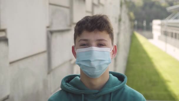 Joyful smiling student in a medical mask on the background of the university building on a sunny day. Back to school concept - Footage, Video