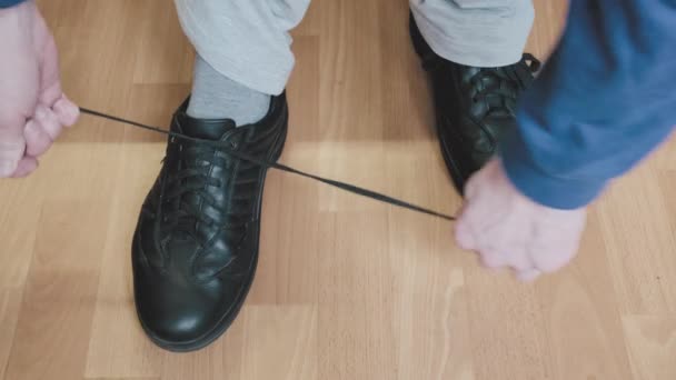 Mann in blauer Jacke und weißer Hose bindet Schnürsenkel seiner schwarzen Schuhe - Filmmaterial, Video