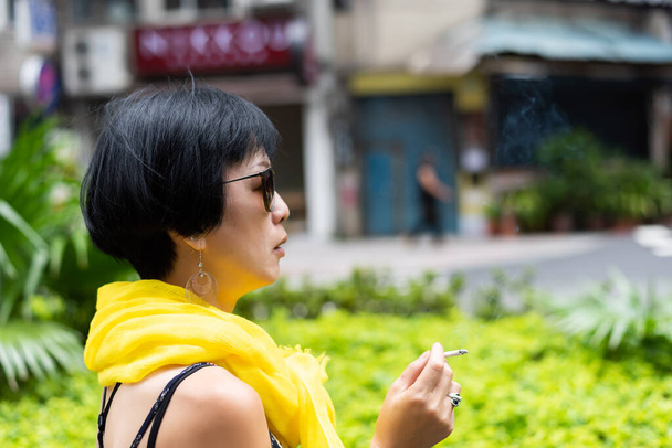 公共の場でタバコを吸っているアジアの女性が - 写真・画像