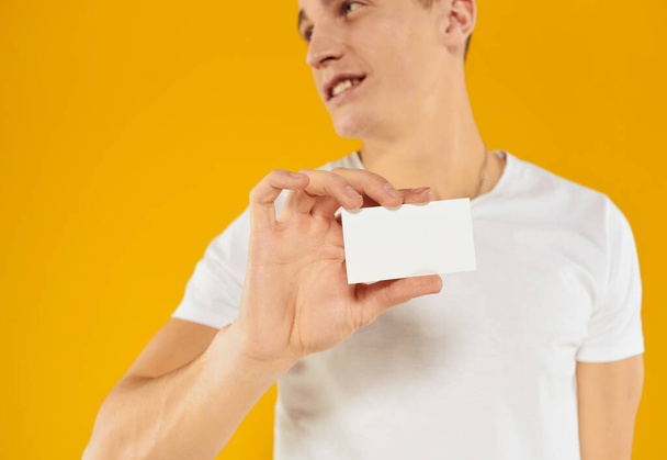 homem em t-shirt branca mostrando cartão de visita no fundo amarelo vista cortada - Foto, Imagem