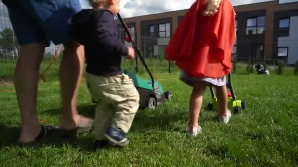 Vater und Kinder mähen Rasen. Papa hat echten Rasenmäher, Tochter eine Spielzeugversion - Filmmaterial, Video