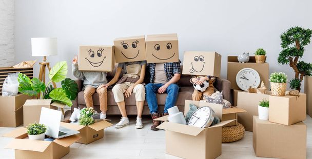 Nierozpoznawalna szczęśliwa rodzina: para i dzieci w kartonowych pudełkach na głowach siedzą razem w nowym mieszkaniu z różnymi rzeczami podczas przeprowadzki - Zdjęcie, obraz