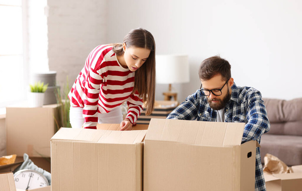 Щаслива сім'я: молодий чоловік і жінка розпаковують картонні коробки з речами під час переїзду в нову квартиру
 - Фото, зображення
