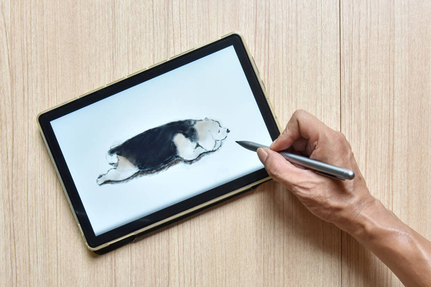 Tabletin çizimi ve tasarımı için yeni bir teknoloji kavramı olan tahta masa üzerinde dijital kalemli av köpeği çizimini gösteren bir tablet. - Fotoğraf, Görsel