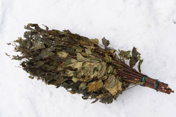 Una escoba para un baño hecho de ramas de abedul yace en la nieve  - Foto, Imagen