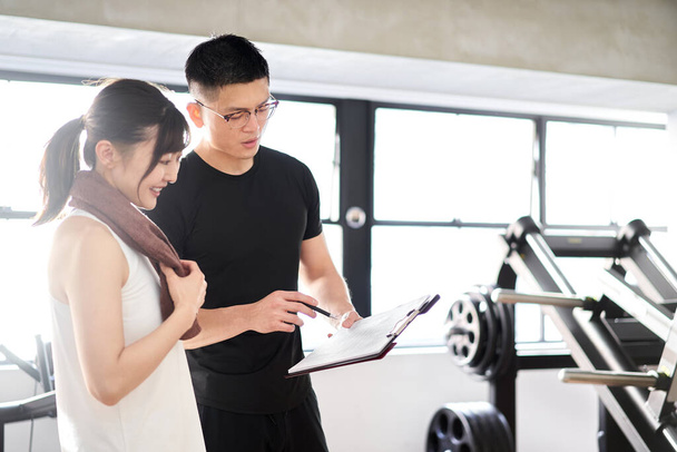 アジア系男性のパーソナルトレーナーがトレーニングアドバイスを行う - 写真・画像