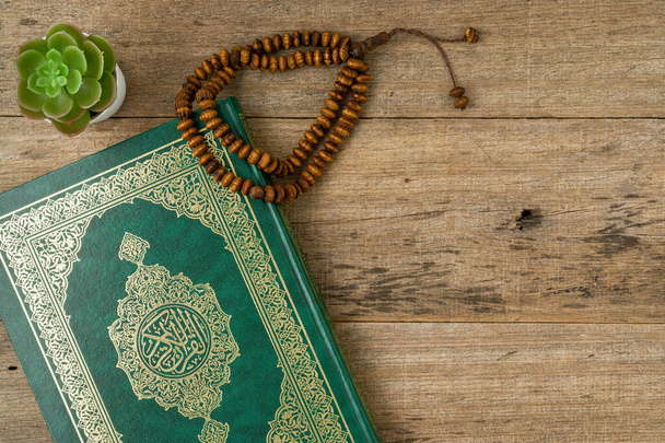 Saint Coran avec calligraphie arabe écrite signifiant Al Coran et perles de chapelet ou tasbih sur fond de planche de bois avec un espace de copie. Pose plate. - Photo, image