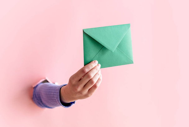 female hand hold green envelope on pink background. - Foto, Imagen