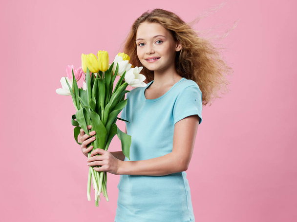 kleines Mädchen mit einem Blumenstrauß Frühling rosa Hintergrund blaues T-Shirt - Foto, Bild