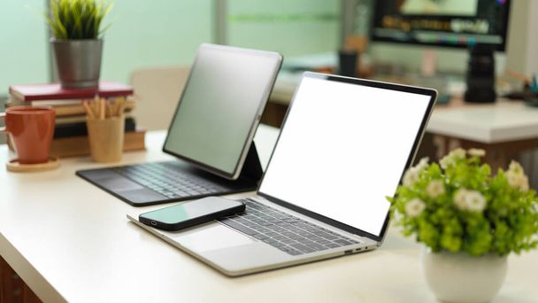 Widok z boku biurka z dwoma laptopami, smartfonem, doniczkami, książkami i zapasami, ścieżka wycinania - Zdjęcie, obraz