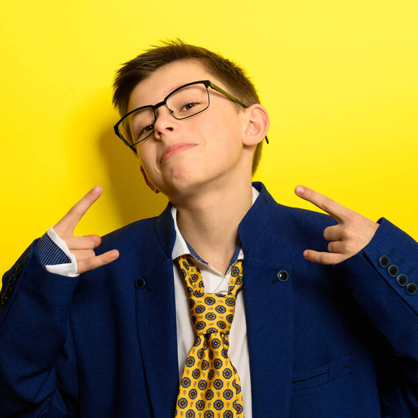 Attractive boy in an adult suit on a yellow background, a child's imagination about adult life. new - Photo, Image