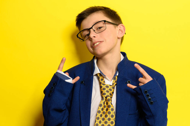 Attractive boy in an adult suit on a yellow background, a child's imagination about adult life. new - Photo, Image