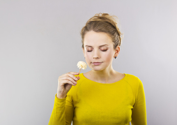 Beautiful blonde with a flower in her hand on a gray background - Photo, Image