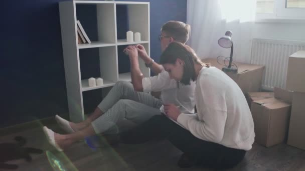 Glückliches Paar bereitet sich auf Umzug vor, Familie sitzt am Umzugstag auf dem Fußboden im Wohnzimmer - Filmmaterial, Video