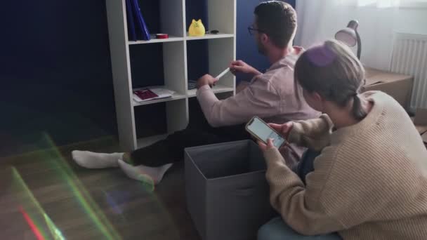 Young couple prepare to moving out relocation, family sitting on floor in living room. Man uses a tape measure to measure the closet - Footage, Video