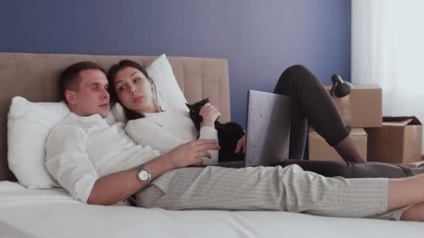 Una coppia felice si rilassa dopo essersi trasferita in una nuova casa. Coppia posa sul letto e guarda lo schermo del notebook - Filmati, video