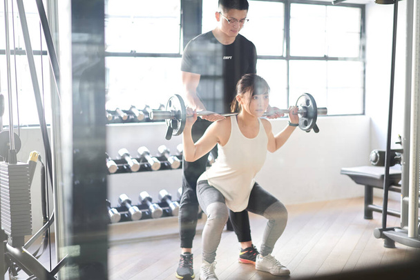Ázsiai nő csinál súlyzó guggol segítségével egy edző - Fotó, kép