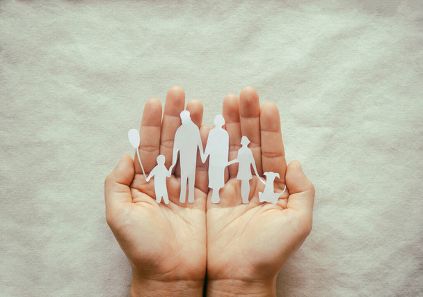 Hand holding family paper cut on fabric background. Family day concept, foster care, domestic violence, homeschool, international day of families, world mental health day, world autism awareness day. - Photo, Image