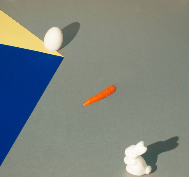 El conejo de Pascua espera una zanahoria y un huevo cayendo por un cubo de papel. Ilusión óptica creativa. Efecto de gravedad sobre fondo colorido. 2021 Resumen Composición de Pascua. - Foto, imagen