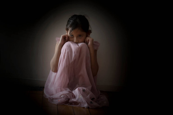 Пояс в руке угрожает печали обиженной маленькой девочке, напуганной. Ребенок, сидящий в темном коридоре перед дверью со светом. Страх и нерешительность. Бытовое насилие в отношении детской концепции. - Фото, изображение