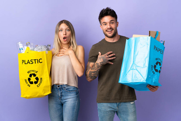Young caucasian couple recycling isolated on purple background surprised and shocked while looking right - Photo, Image