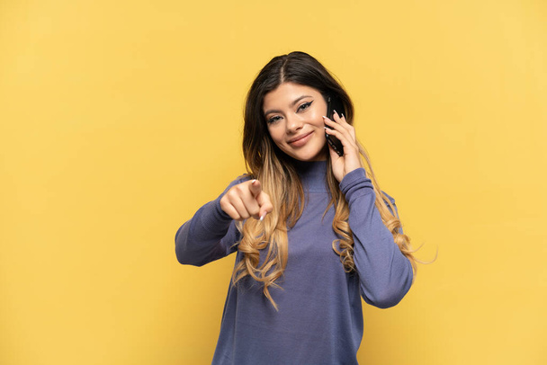 Young Russian girl using mobile phone isolated on yellow background showing and lifting a finger - Photo, Image