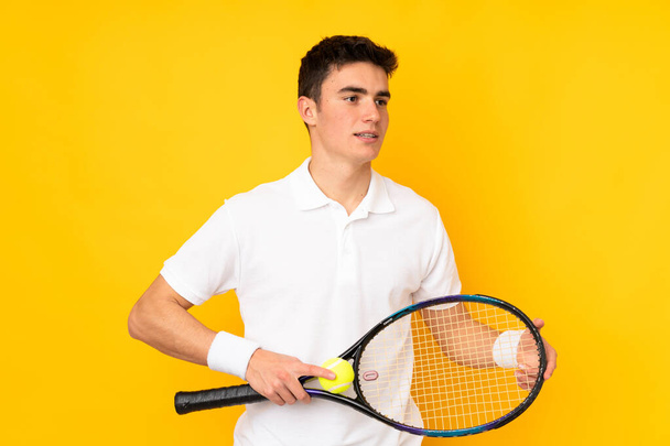 Handsome teenager tennis player man isolated on yellow background playing tennis - Fotoğraf, Görsel